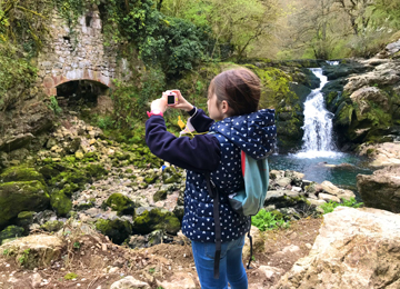 Una niña con un cámara de otos y la cascada Ixkier al fondo